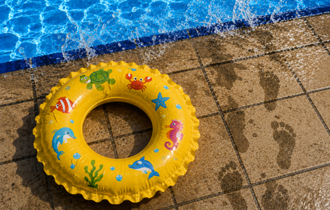 Children's inflatable swim ring beside a Rhode Island community swimming pool with wet footprints and water splashes illustrating swimming pool safety and biological contamination prevention.